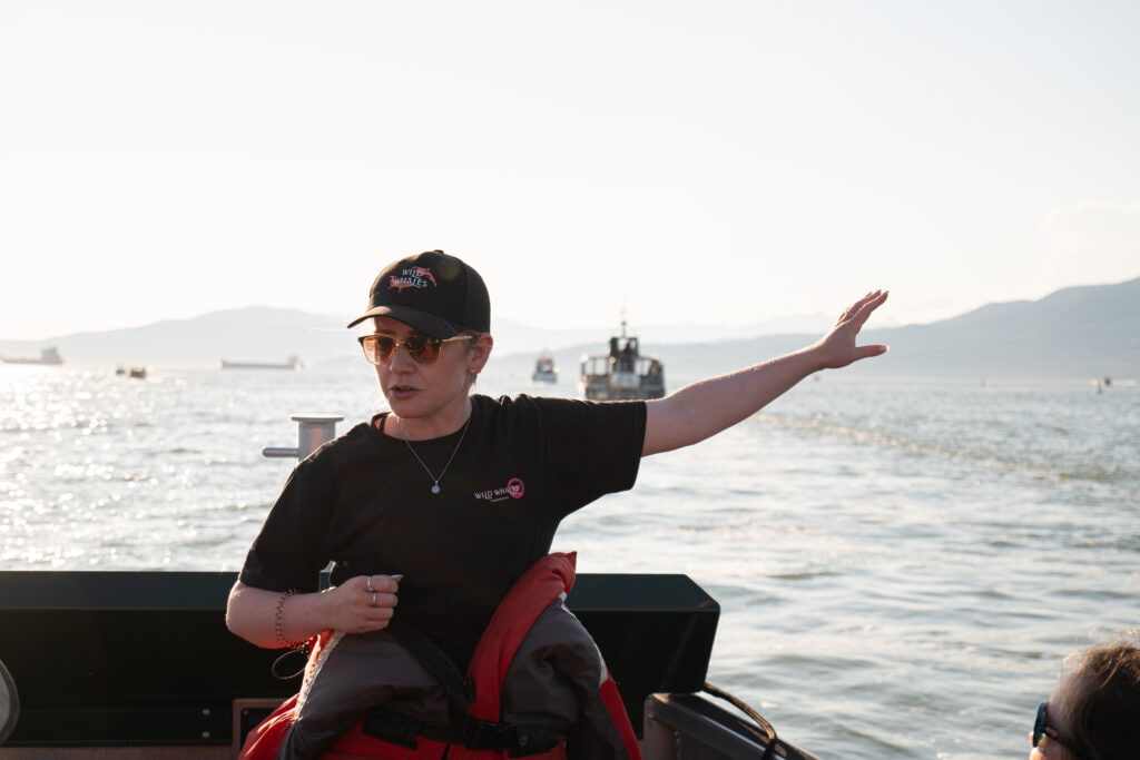 A naturalist gives information to a group of guests on a whale watching tour with boats in the background